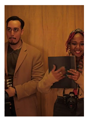 Sepia photo of a man with a mustache wearing a suit and a woman with a camera and a large notebook.