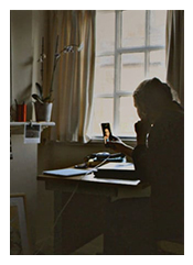 Outline of a woman sitting by a window, in front of a desk, looking at a photo in her hands.